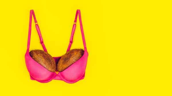 Two coconuts in bright pink bra on yellow background. Woman breast metaphor. Plastic surgery,
